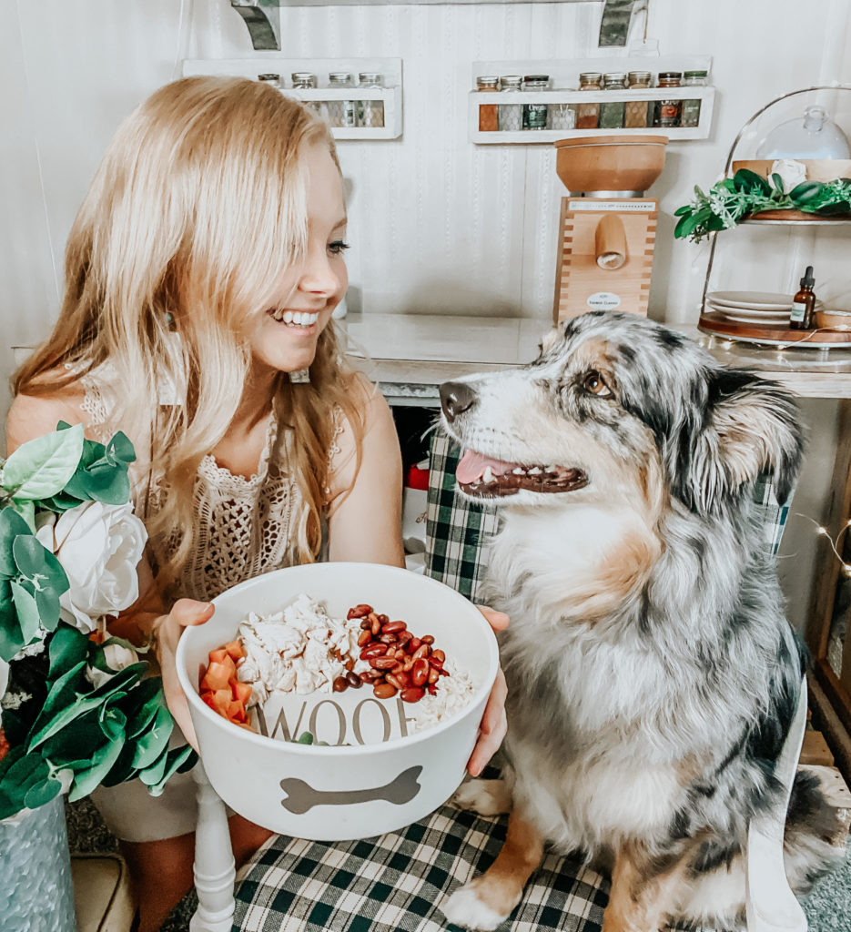 blonde girl (kiersten zile) looking at her australian shepherd face to face holding homemade dog food in a bowl that says woof