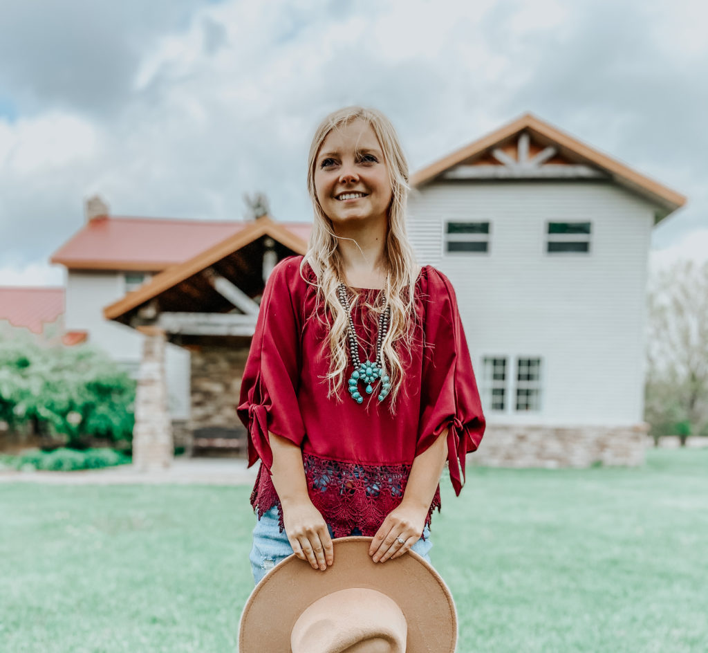 a blonde girl (Kiersten Zile) in front of a small Inn with a turquoise jewelry piece (squash blossom necklace) with red blouse and silver navajo necklace
