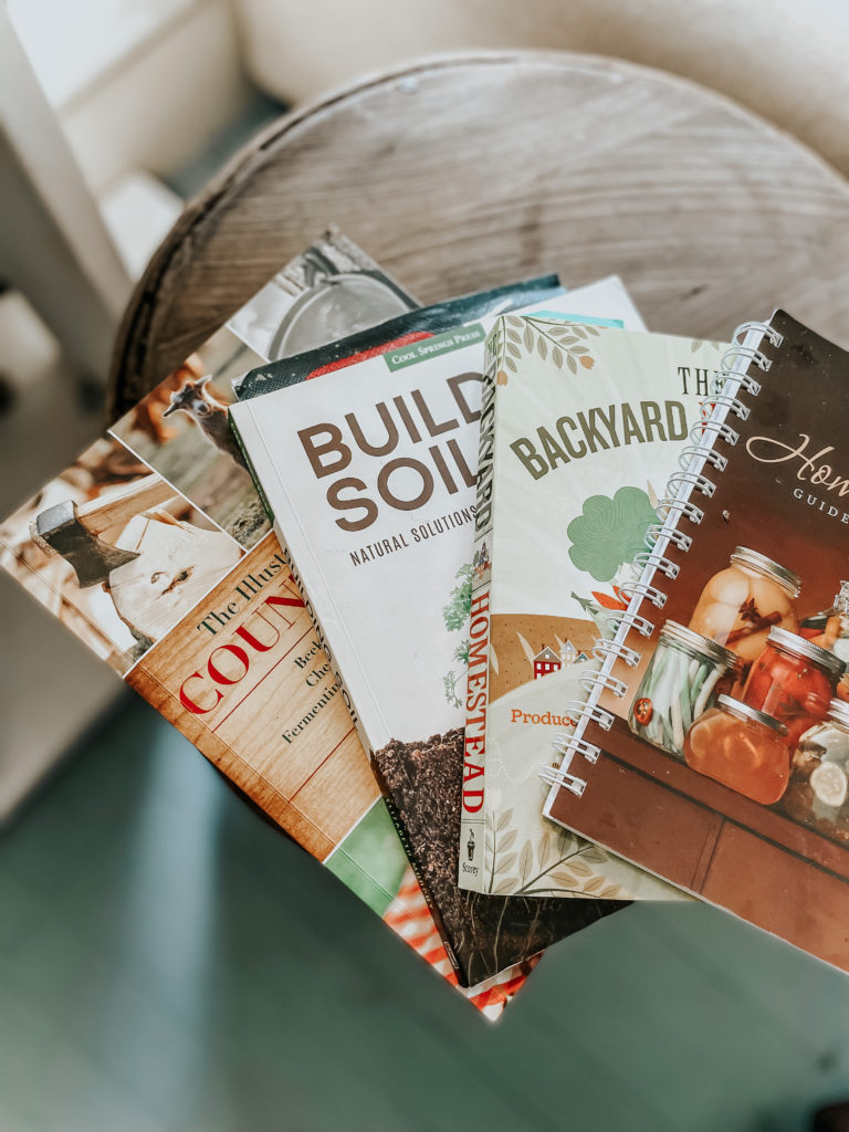a stack of best homesteading books laid out on a wood barrel in a bright white living room