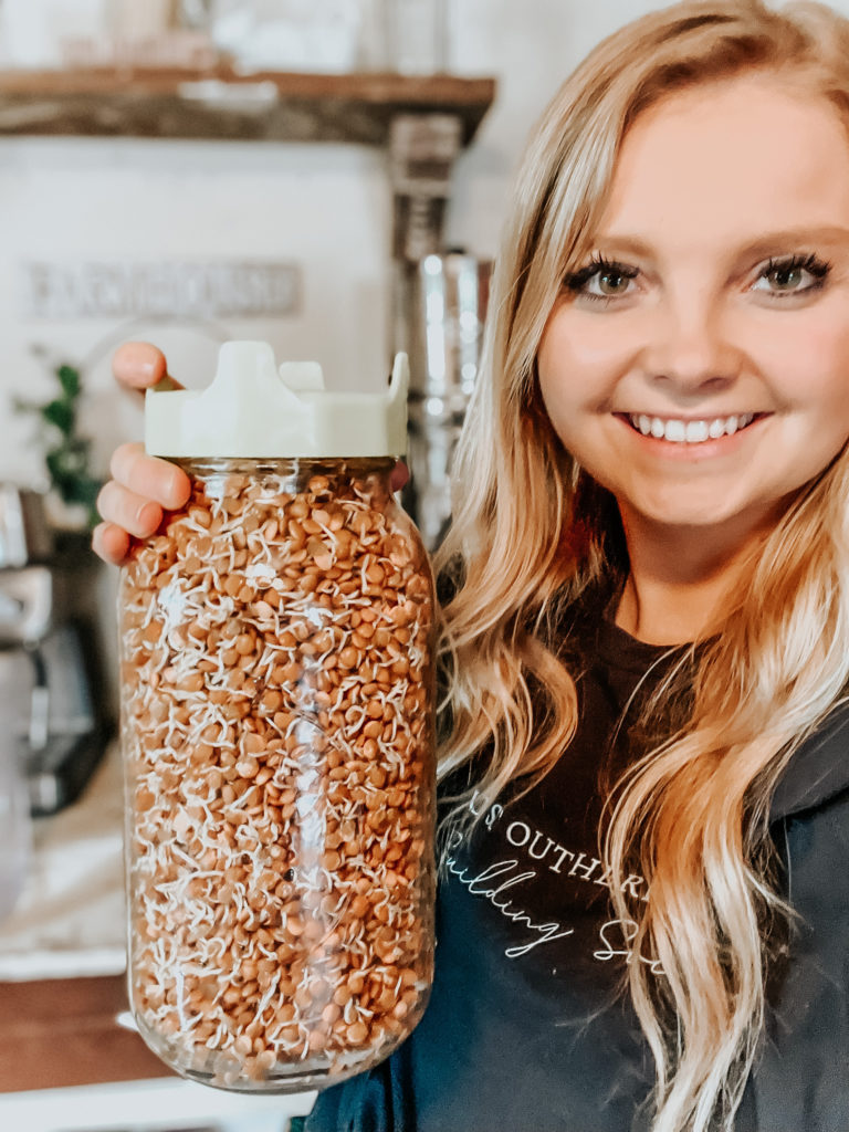 kiersten zile holding a half gallon mason jar with sprouted beans and lentils with a shirt that says building soil