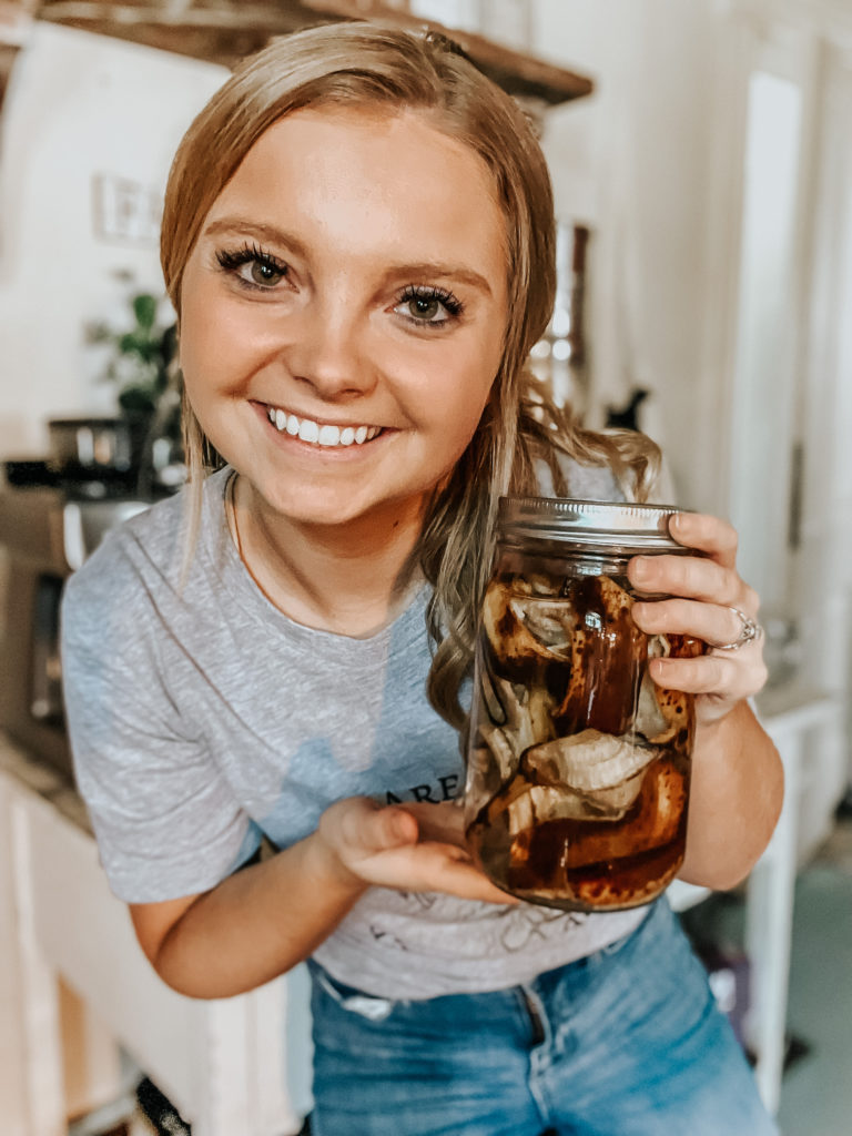kiersten zile holding a mason jar of banana peel fertilizer with a shirt that says farming, food, and health are all interconnected