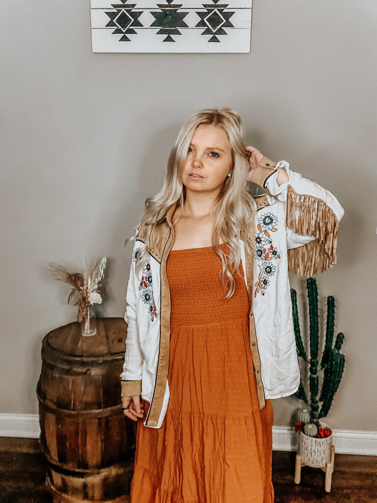 kiersten zile holding her hair up with a fringe western button-up and a burnt orange dress to show the western fall dress style to give a visual of the look