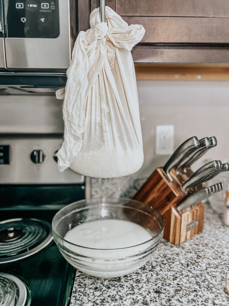 draining all of the whey from the ricotta cheese curds by hanging the cheesecloth on a cabinet door with a mixing bowl catching the whey liquids underneath