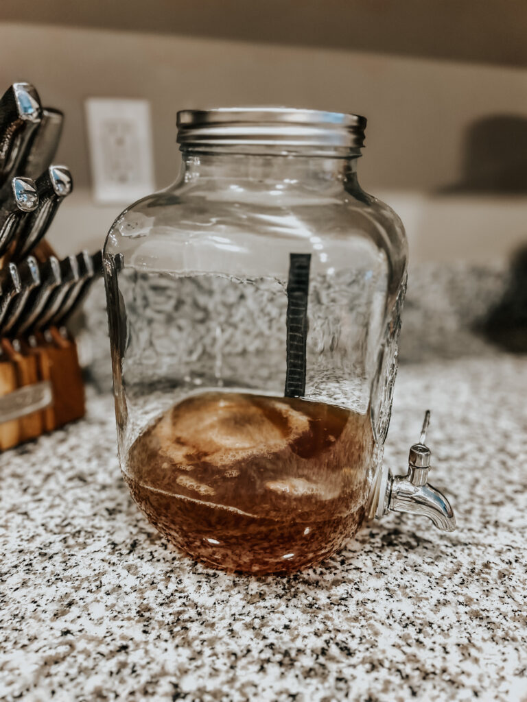 kombucha with SCOBY showing in a continuous kombucha brewing jar with a thermometer